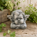 Statue of a cherub with wings on a wooden surface with greenery in the background