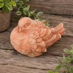Terracotta-colored bird figurine concrete statue on a wooden surface with plants in the background